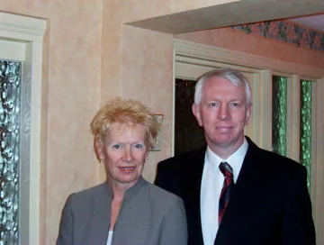 Pam and Iain standing together indoors, dressed smartly for an evening out.