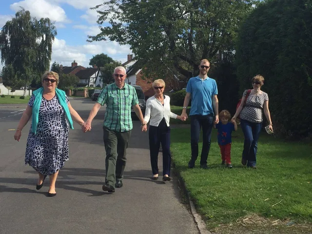 Iain and Pam walking hand in hand with family along a village street.