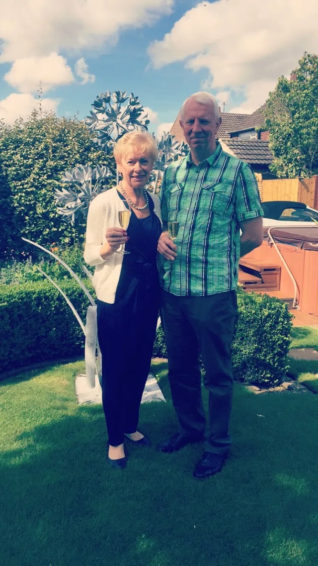 Iain and Pam raising a glass of champagne together in a sunny garden.