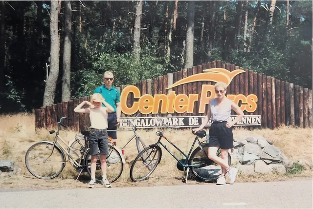 The family standing with bicycles beside a Center Parcs sign in the Netherlands on a sunny day.