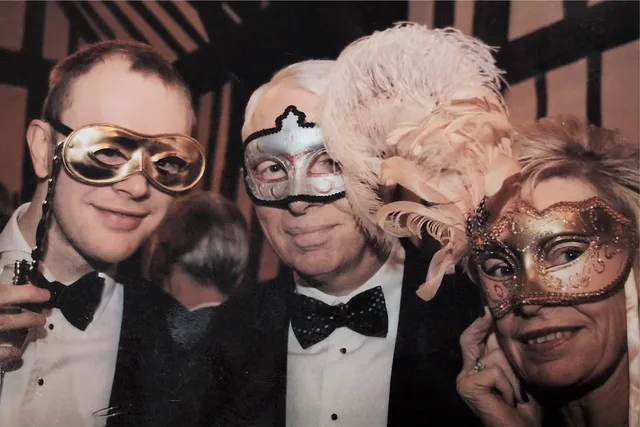 Iain wearing a silver masquerade mask at Erica's 50th birthday party, flanked by two friends in matching masks.