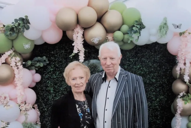 Pam and Iain standing beneath a floral and balloon arch at Evelyn's naming day.