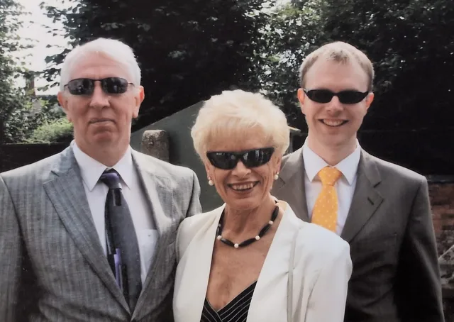Iain, Pam and Euan, all wearing sunglasses, in a garden at Thomas's christening.